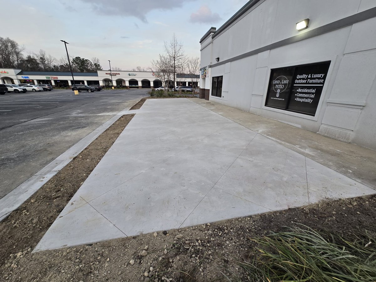 Concrete sidewalk and parking lot outside a modern commercial building with signage on the white exterior wall