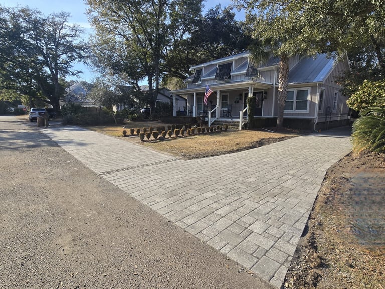 Gray house with solar panels on roof and paved driveway lined with landscaping stones, surrounded by trees on a residential street