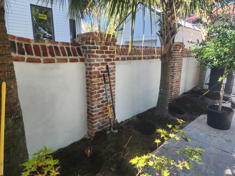 Brick planter boxes with white sides surrounding a palm tree in a paved garden area with green vegetation