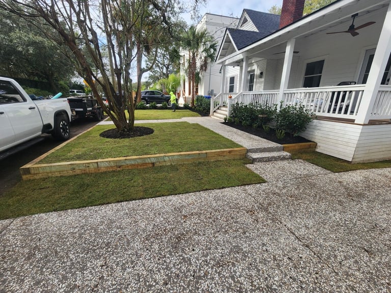 White single-story house with front porch, manicured lawn, and gravel driveway, parked white car visible on left side