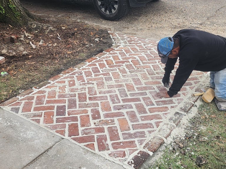 Worker in blue cap installing red brick patio in herringbone pattern on residential driveway
